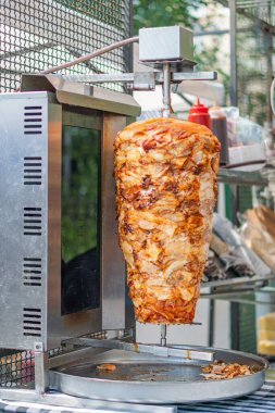 Şiş kebap hazırlayan mutfak sahnesi, yanan fırın, kırmızı sos şişesi ve kağıt havlular. Parlak ışıklandırma, samimi tarz, mesaj yok.