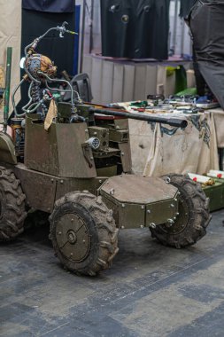 Endüstriyel atölyedeki küçük yeşil tank benzeri robot gelişmiş sensörler, büyük lastik izleri ve sağ ön taraftan görünen birden fazla yapay ışıklandırma.