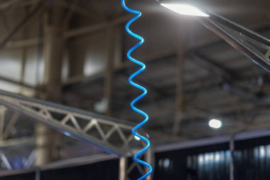 Bir pencere ya da tavan penceresinden gelen doğal ışığın arka planına karşı mavi spiral ışık yayan metal tırtıklı bir yapıya sahip kapalı bir sahne, görüntü bir hareket ve enerji duygusunu tasvir eder.