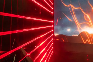 Kırmızı ışık desenli lazer gösterimi karanlık bir arkaplan üzerinde geometrik desen oluşturur. Ekran, bir video oyunundan veya sağ tarafta animasyondan dinamik içeriği gösterir.