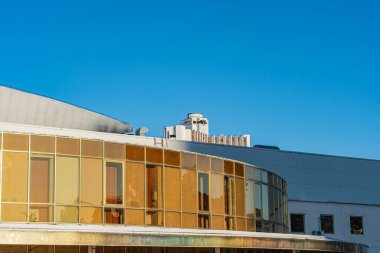 Eğri yüzlü modern mimari yapı, altın renkli fayanslar, büyük pencereler, doğal ışık, sıcak aydınlatma ve ayırt edici tasarım elementleri.