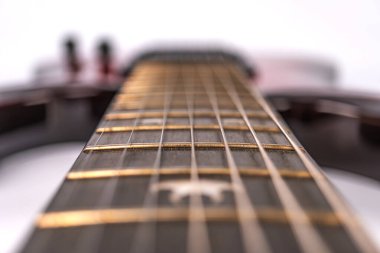 Görünür telleri olan ahşap bir elektro gitar boynunun yakın çekimi, açılı görünüm fretboard eğriliği ve sicim hizasını gösteriyor doğal sıcak kahverengiler renk paletine hakim, yumuşak gölgeli