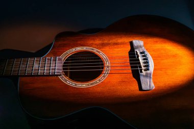 Karanlık, parlak akustik bir gitarın altı teli ve maun veya benzeri bir ağaçtan yapılmış iki pikapı ile yakın plan çekimde, görünmeyen perdeleri olmayan serbest bir parmaklık içerir.