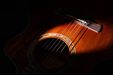 Koyu kahverengi akustik gitarın yakın plan görüntüsü, vücuduna ve tellerine odaklanmış, kenarın etrafındaki daha hafif ahşap aksanlar.