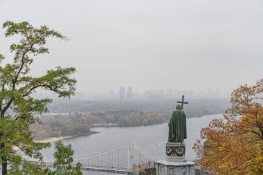 Prens Vladimir 'in heykeli, iki köprüsü olan şehir manzarası modern süspansiyon ve tarihi taş, sonbahar yaprakları, ağaçlar, bulutlu gökyüzü, fl Kyiv, Ukrayna - 24 Ekim 2025
