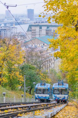 Kyiv füniküler, tramvay yükselen tepe, sonbahar manzarası, şehir manzarası, kırmızı çizgili mavi ve beyaz tramvay, iki araba, sarı ve turuncu ağaçlar, dağınık yapraklar, Kyiv, Ukrayna - 24 Ekim 2025