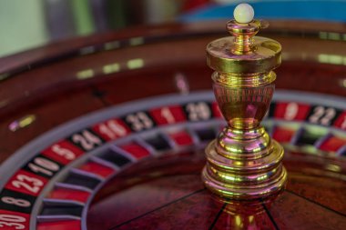 Hareketli rulet tekerleğinin yakın plan görüntüsü, karanlık ahşap bir tabana karşı, karmaşık altın şehir manzarası modeli dramatik gölgeler ve iç çalışmalara odaklanma beklenti yaratır.