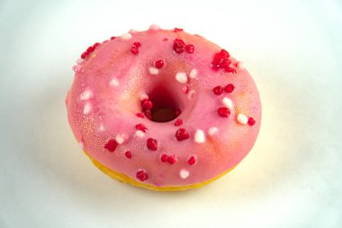 Tek bir pembe jöleli donut, muhtemelen kızarmış, beyaz arka planda kırmızı serpinti tohumları, parlak ışıklandırma, yumuşak bir gölge doğrudan perspektif, metin veya ek bağlam yok