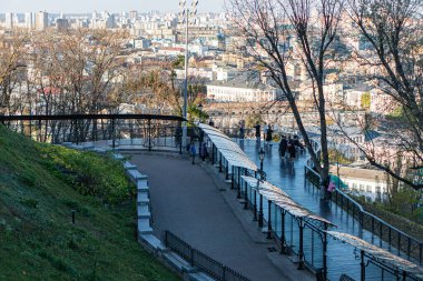 Ağaçlar ve çimlerle kaplı, solda banklar bulunan şehir manzaralı Kyiv parkı manzarası. 3 Kasım 2025 Ukrayna 'nın başkenti Kyiv' de basamaklar ve yükseltilmiş bir yürüyüş var.