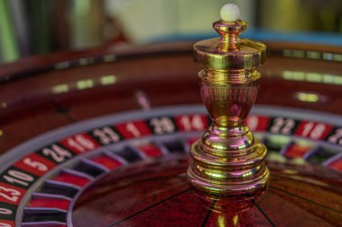 İçi bulanık bir kumarhanede dönen rulet masasının yakın çekimi, 0 ile 36 arasında değişen kırmızı ve siyah yuvaları var, iki yeşil sıfır dahil, sabit beyaz top gösteriyor ki