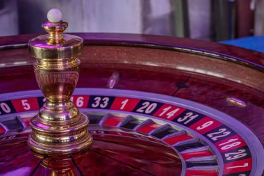 Kumarhanedeki rulet tekerleğinin yakın plan görüntüsü, alternatif kırmızı ve siyah numaralandırılmış panelleri olan, altın renkli bir küre altında ışıklandırma ayrıntıları arttırır.