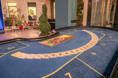 Canlı bir kumarhane oyun masasına yakın çekim, yarış pisti şeklinde, mavi bir bez ve dağınık iskambil kağıtları ile çevrili oda sofistike göstermektedir.