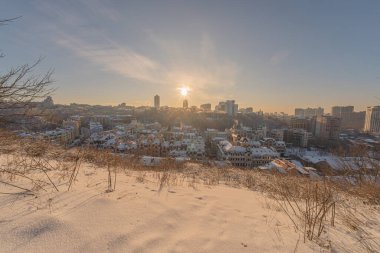 Günbatımında Kiev 'in kış manzarası Karlı şehir silueti, çıplak bitki örtüsü ile tepe, turuncu gün batımı, açık mavi ile koyu gri gökyüzü, zıt aydınlatma, yüksek binalar