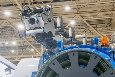 Büyük, mavi endüstriyel bir makine geniş bir fabrika zeminine ve güvenlik bariyerlerine hükmediyor makine çeşitli mekanik bileşenleri içeriyor dişliler, kollar, muhtemelen hidrolik pnömatik sistemler gibi.