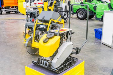 Açık motorlu, sarı kazıcılı, gri platforma monte edilmiş, daha küçük yeşil-sarı engebeli arazi makinesi ve işaret edilen filo Ar