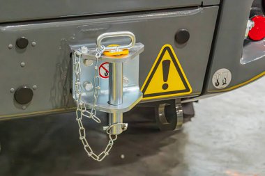 Olası bir otobüsün yakın görüntüsü, üzerinde ünlem işareti olan sarı-siyah bir uyarı cihazı gösteriyor. Cihaz beyaz gri bir araçtaki metal bir çubuğa bağlı.