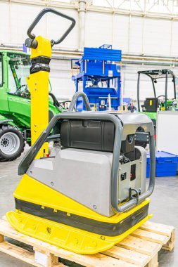 Özet sarı forklift yoğun bir endüstriyel ortamda park halinde, biri sağdan sola hareket eden yeşil traktörler, diğeri de sağdaki beton zemin etkin mavi palet.