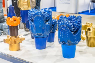 Endüstriyel hidrolik ekipmanların yer aldığı ticaret fuarı ön planda büyük, mavi vites benzeri bir parça var, arka planda iki küçük parça var. Sarı silindirik nesneler boru tipi.