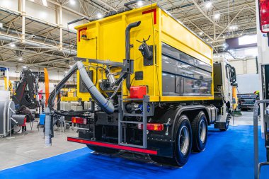 İçerde, kırmızı arka farları ve yan aynaları olan canlı sarı atık toplama aracı mavi halılı zemin lastiklere doğru gidiyor başka bir yere açılan kapı işaretleri sırt çantasındaki diğer objeler