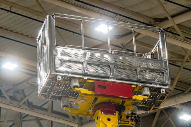 Sarı tabanlı, metal çitli, bariyerli, sanayi tipi geniş bir makine. Kanal işi, borular ve üstten aydınlatma ile endüstriyel bir ortamda yer alıyor. İşaret ya da marka yok.