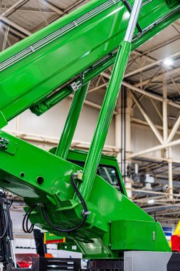 Büyük yeşil bir inşaat aracı, muhtemelen bir hangarda ya da depoda. Bakım ya da teftiş için kaput, yüksek tavanlı geniş bir iç mekan ve floresan aydınlatma tarzı.,