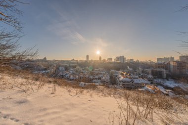 Kış mevsiminde Ukrayna, Kiev 'in karla kaplı tepe manzarası çeşitli mimari çeşitliliğe sahip Sunlit şehri, karşıt mavi gökyüzü, turuncu bulut, Stark ağaç siluetleri, belirgin merkez bina, çıplak dallar,