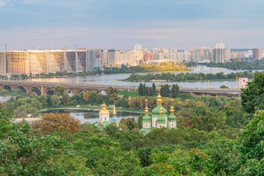 Ukrayna 'nın başkenti Kyiv, Ukrayna' nın güneş doğarken veya batarken mavi nehir ve yemyeşil alanlara karşı altın bir kubbe bulunan önemli beyaz bir bina.
