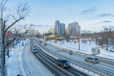 Çok şeritli otoyolu olan karlı Kyiv şehir manzarası, çeşitli araçlar, trafik veya olay, soğuk hava, karla kaplı zemin ve çatılar, ağaçlar, uzak apartman binası Kyiv, Ukrayna - 17 Şubat 2026