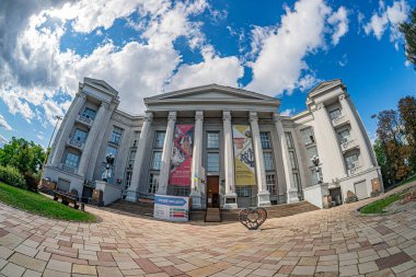 Kyiv, Ukrayna 'da sütunları ve pedikürleri olan klasik bina, doğal ışık, bisiklet, ekran dışında yürüyen kişi, parçalı bulutlu gökyüzü, açık kaplıca Kyiv, Ukrayna - 18 Ağustos 2025