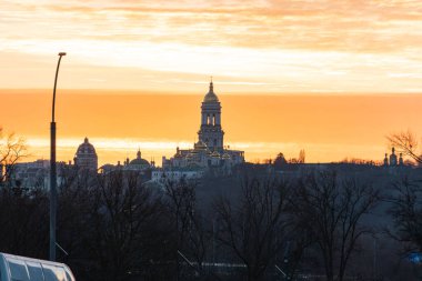 Kyiv, Ukrayna 'nın seçkin kulesi ve ağaç siluetleri, çarpıcı gökyüzü, sıcak parıltı, çatılar, kemerli mimari, Kyiv, Ukrayna - 13 Aralık 2025