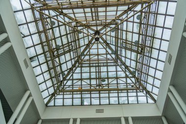 Unique yellow geometric ceiling design in a rectangular white room with large windows, emphasizing natural light and a distinctive perspective from below