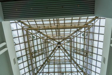 Overhead view of a warm, earth-toned interior with a geometric wooden ceiling structure and numerous rectangular windows