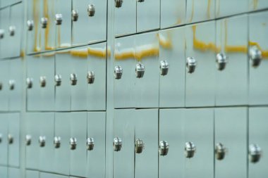 Metalin değişik tonlarından ya da boyanmış griden yapılmış birden fazla posta kutusunun yakın plan görüntüsü her posta kutusunun bir sapı ve anahtar deliği vardır, girintili üstlerle eşit olarak düzenlenmiş hatta aydınlatma şekeri bile