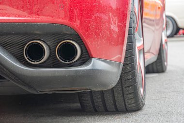 İyi bakımlı kaportası ve görünen egzoz boruları olan kırmızı bir spor arabanın yakın plan çekimi. Tekerleğin çok dilli bir tasarımı var, muhtemelen piyasa güncellemesi ve arka plan Kyiv, Ukrayna 10-12-2024