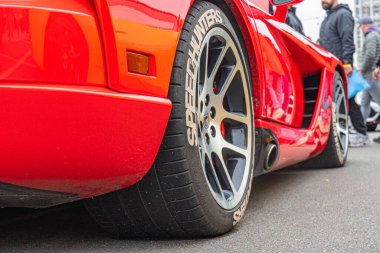 Üstü açık kırmızı spor bir arabanın yan profil çekimi. Parlak aerodinamik stili, krom aksanlı siyah tekerlekler ve beş dilli ayırt edici tasarım. Kyiv, Ukrayna 10-12-2024