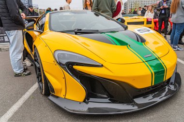 Yarış çizgileri olan canlı sarı bir McLaren spor arabası, bir pistte park halinde, muhtemelen bir etkinlikte ya da toplanırken insanlar arka planda Kyiv, Ukrayna 10-12-2024
