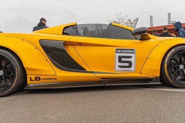 Ayırt edici tasarımı olan parlak sarı, yüksek performanslı spor bir araba, 5 numara ve LDM logosu, bulutlu gökyüzü Kyiv 'in ortasında beton bir yüzeye park edilmiş, Ukrayna 10-12-2024