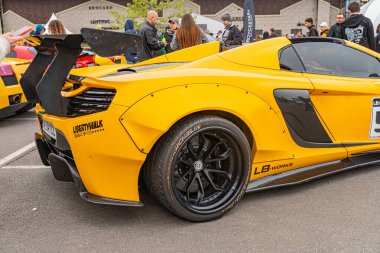 Sarı bir Lamborghini halka açık bir sokakta ya da otoparkta park halinde, diğer araçlar ve arka planda insanlar var. Olay yeri, Ukrayna 'nın Kyiv kenti yakınlarında bir açık hava olayı ya da toplanma olduğunu gösteriyor.
