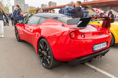 Aerodinamik kıvrımlı kırmızı bir spor araba, büyük siyah tekerlekler ve arka kanatçıklar bir araç etkinliğinde gün boyunca çekilmiş gizli bir görüntüde sergileniyor.