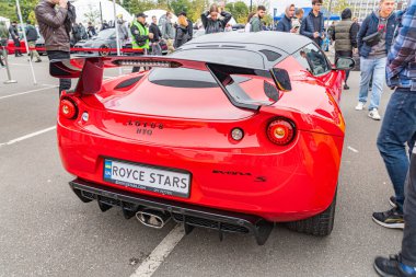 Kırmızı, yüksek performanslı bir spor araba, muhtemelen bir Bentley, ziyaretçilerin geçtiği bir açık hava etkinliğinde park edilmiş, ve benzersiz plakalarında BENTLEY STARS yazıyor. Araba ha Kyiv, Ukrayna 10-12-2024