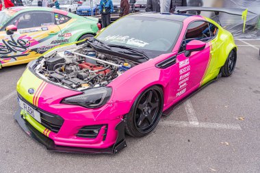 Modifiye edilmiş bir yarış arabasının bulanık bir görüntüsü, muhtemelen bir olay veya sergide, iki renkli pembe ve sarı renkte, kapalı alanda görünür ama odak noktasında T Kyiv, Ukrayna 10-12-2024 değil.