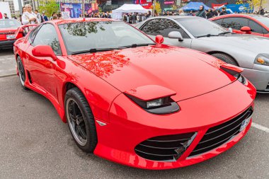 Kırmızı bir spor araba, aerodinamik tasarım ve hız yeteneklerini sergileyen bir açık hava sergisinde ya da gösteride belirgin bir şekilde sergilenir. Araç büyük hava girişlerine sahiptir, Mul Kyiv, Ukrayna 10-12-2024