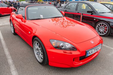 Siyah yarış çizgileri olan canlı kırmızı bir spor araba, bir caddeye park edilmiş. Arabanın vücut rengi yan aynaları ve arka spoyeri var. Aerodinamik Licens Kyiv, Ukrayna 10-12-2024