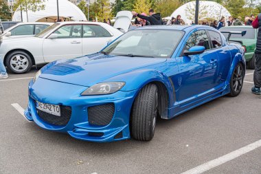 Aerodinamik modifikasyonlara sahip mavi bir spor araba, bir şehir ortamında asfalt bir yüzeye park edilmiş. Aracın zarif bir tasarımı ve çok dilli arka pazar tekerlekleri var. Oth Kyiv, Ukrayna 10-12-2024