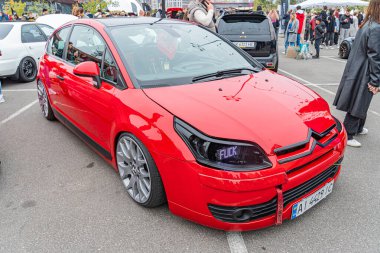 Kırmızı bir spor araba, bir açık hava otomobil fuarında çapraz konumlandırılmış, büyük bir arka spoiler, geniş gövde çamurlukları gibi ayırt edici değişiklikler sergiler, ve benzersiz tampon tasarımı Kyiv, Ukrayna 10-12-2024