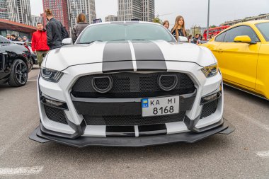 Beyaz, özel boyanmış, siyah ve kırmızı çizgili, aerodinamik bileşenleri olan bir Ford Mustang spor arabasının yakın plan görüntüsü, açık bir park alanında veya Ukrayna 10-12-2024 sergi salonu Kyiv, Ukrayna