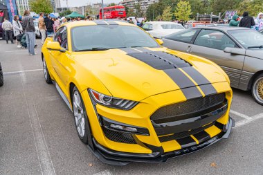 Siyah aksanlı sarı Ford Mustang spor arabası asfalt bir yüzeye park edilmiş, kaput ve arka tarafta koşan kamera karakteristik siyah çizgiler Kyiv, Ukrayna 10-12-2024