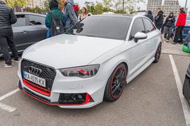 Siyah ve kırmızı aksanlı beyaz bir Audi arabası gayri resmi bir ortamda gösteriliyor, muhtemelen bir araba fuarında ya da buluşmada. Görüntü gösteriyor ki birden fazla kişi Kyiv, Ukrayna 10-12-2024 'e hayran.