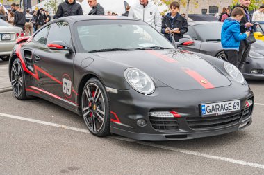 Siyah ve kırmızı bir Porsche 911 GT2 RS halka açık bir yolda ya da otoparkta, izleyiciler etrafında toplanmış olan görüntü benzersiz tasarım elemanlarına odaklanıyor ve Kyiv, Ukrayna 10-12-2024 'e bölünüyor.