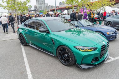 Modifiye edilmiş bir BMW spor arabası süspansiyonu indirmiş, bina ve ağaçların arasında asfalt bir zemine park etmiş jantlar Kyiv, Ukrayna 10-12-2024 ile parlak turkuiseteal bir araba.